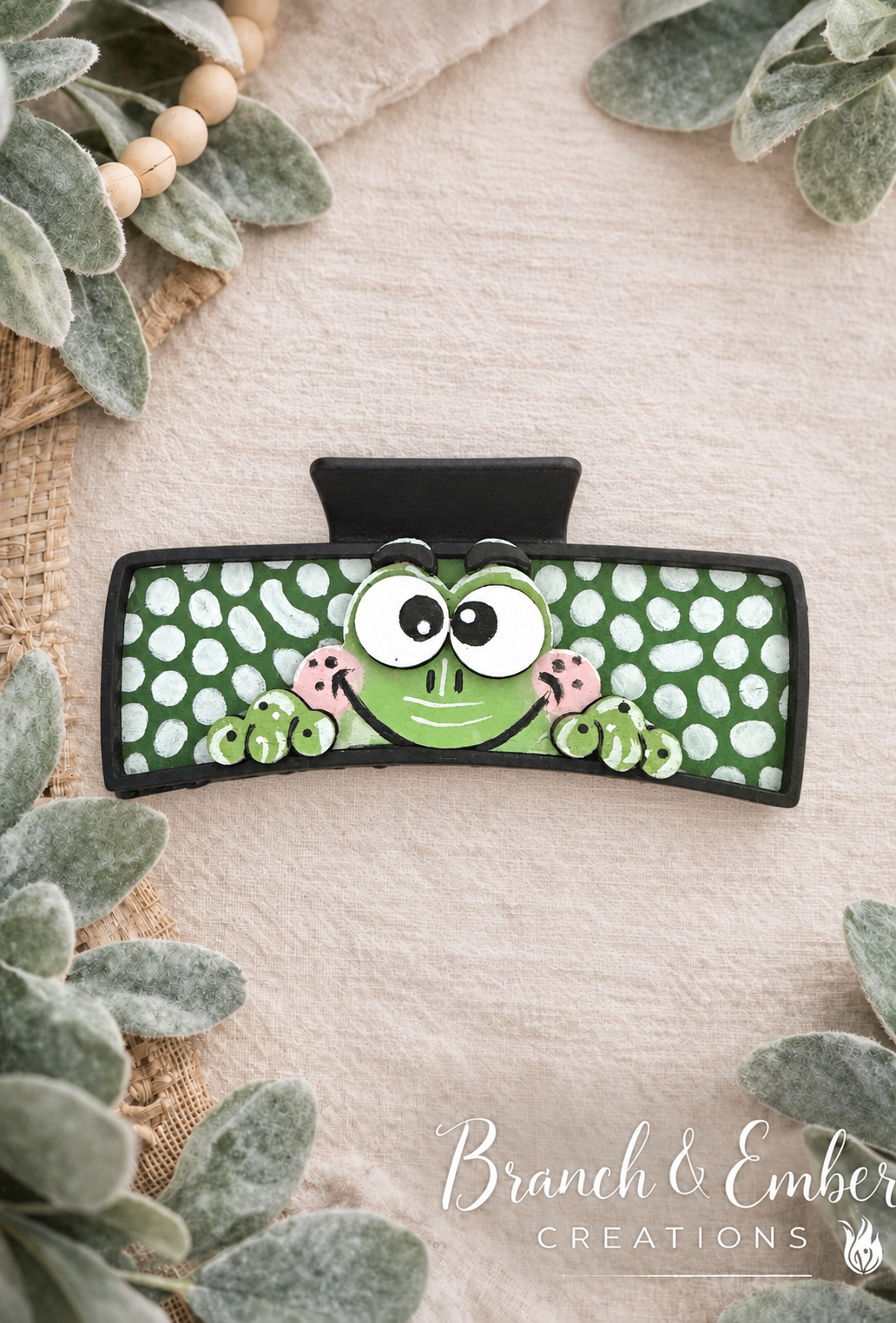 Hand-painted green frog hair claw clip with white polka dots on the Branch & Ember linen and lamb’s ear backdrop