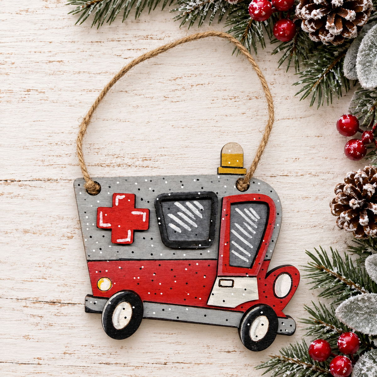 Ambulance ornament on whitewashed wood with evergreen branches and berries