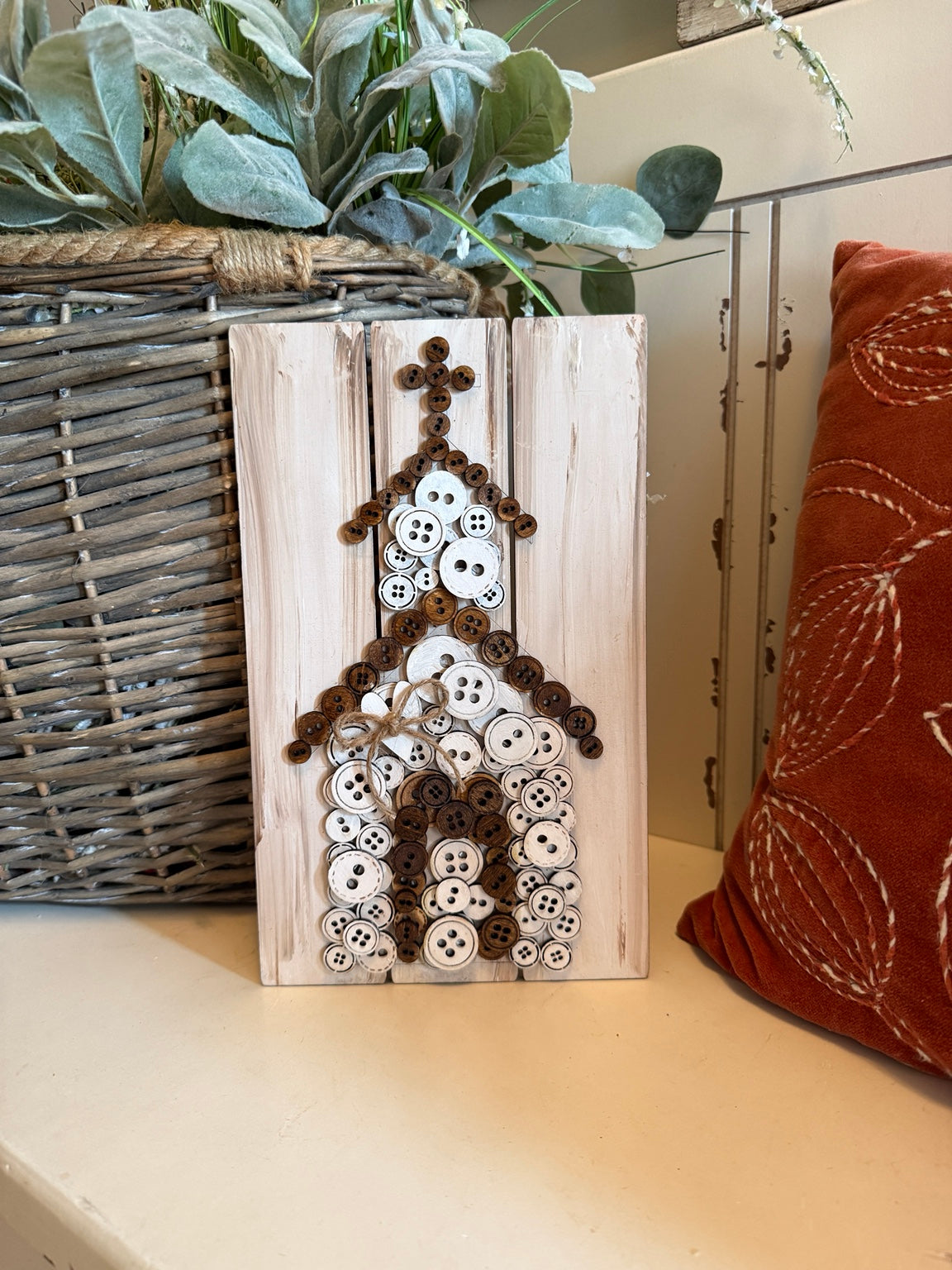White and brown button art church with a twine bow on distressed whitewashed wood.