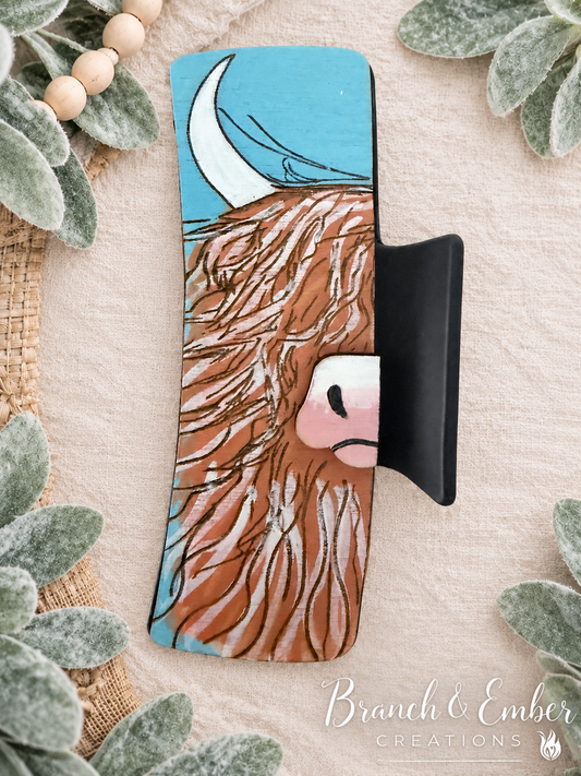Hand-painted shaggy Highland cow wooden hair claw clip with turquoise background on linen and lamb’s ear backdrop